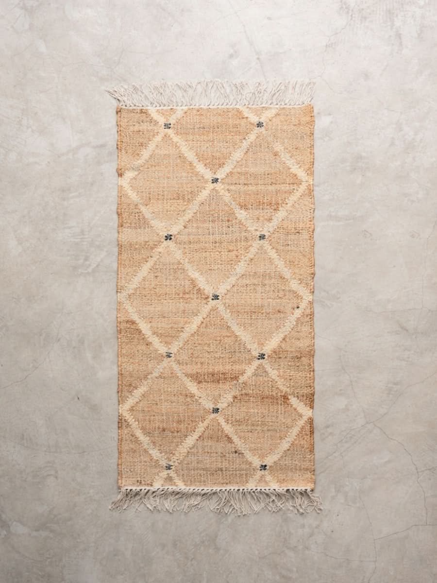 Beige jute rug with diamond pattern and fringe detail on a concrete floor.